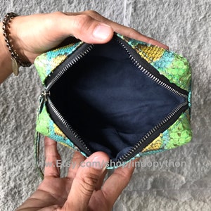 Może przedstawiać: Mała, zielona, niebieska i ż&oacute;łta sk&oacute;rzana torebka typu clutch ze zapięciem na zamek błyskawiczny. Torebka jest otwarta, a wnętrze wyłożone jest ciemnoniebieską tkaniną.