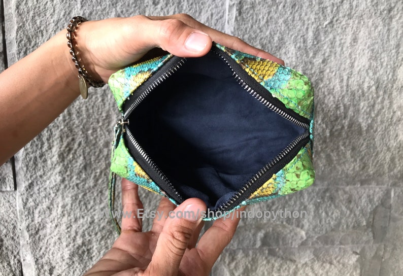 Może przedstawiać: Mała, zielona, niebieska i ż&oacute;łta sk&oacute;rzana torebka typu clutch ze zapięciem na zamek błyskawiczny. Torebka jest otwarta, a wnętrze wyłożone jest ciemnoniebieską tkaniną.