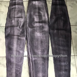 May include: Three pieces of dark gray python skin, each with a different length. The skin has a textured pattern and is folded in a stack.