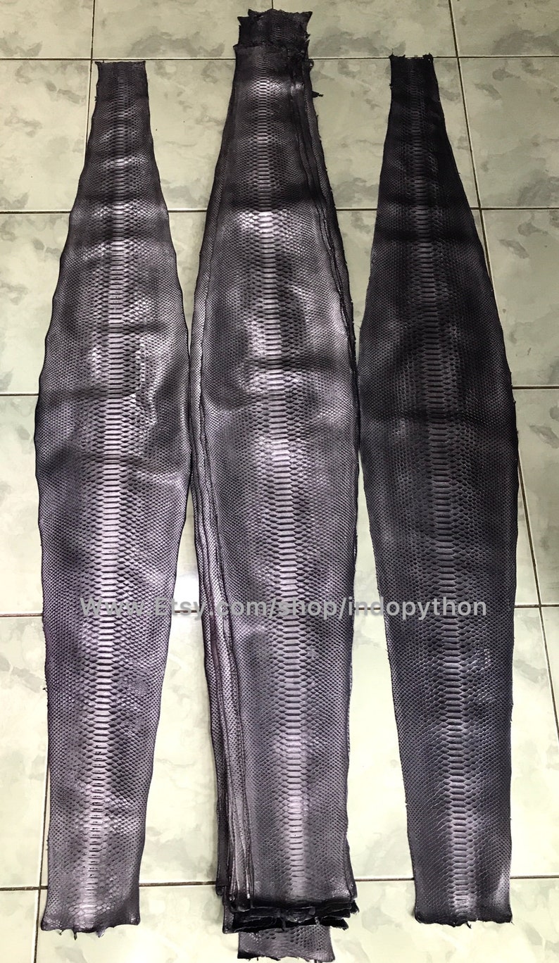 May include: Three pieces of dark gray python skin, each with a different length. The skin has a textured pattern and is folded in a stack.