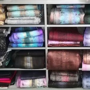 Może przedstawiać: P&oacute;łka z wieloma rzędami ułożonych na sobie sk&oacute;r węża w r&oacute;żnych kolorach i wzorach. Sk&oacute;ra jest ułożona w spos&oacute;b schludny i uporządkowany.