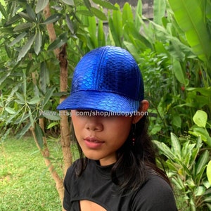 May include: A blue baseball cap made of python leather. The cap has a scaly texture and a shiny finish. The text "www.Etsy.com/shop/indopython" is visible on the brim of the cap.