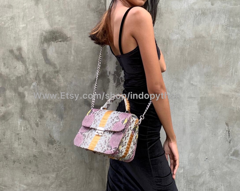 May include: A small, pink, yellow, and white snakeskin handbag with a silver chain strap. The bag has a top handle and a flap closure.