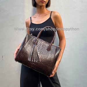May include: A brown leather handbag with a snakeskin pattern and a tassel. The bag has a top handle and a shoulder strap.