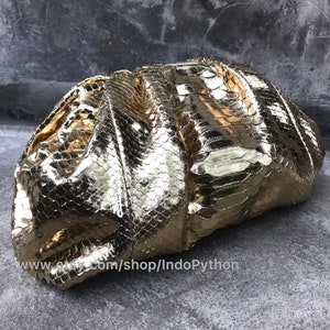 Op de afbeelding: Een gouden clutch gemaakt van pythonskin. De clutch is geplooid en heeft een getextureerd, schubbig oppervlak.