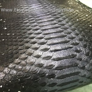 Op de afbeelding: Close-up van zwart pythonleer met een wit splatter-verfdesign. Het leer heeft een textuur, schubbige oppervlak.