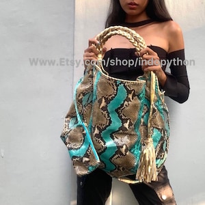 May include: A turquoise and brown snakeskin handbag with a gold braided handle and tassel. The bag is held by a person wearing a black off-the-shoulder top and black pants. The text "www.Etsy.com/shop/indopython" is visible in the image.