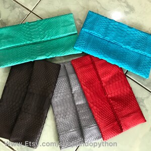 Peut inclure: Plusieurs pochettes pli&eacute;es de couleurs vives. Les pochettes sont de couleur sarcelle, turquoise, rouge, grise et marron. Elles pr&eacute;sentent une texture de peau de reptile. Les pochettes sont dispos&eacute;es sur une surface claire.