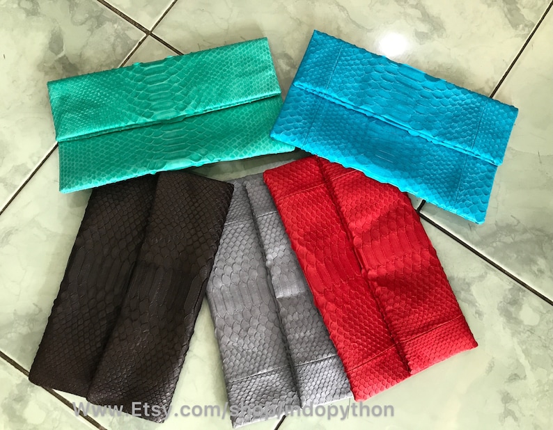 Peut inclure: Plusieurs pochettes pli&eacute;es de couleurs vives. Les pochettes sont de couleur sarcelle, turquoise, rouge, grise et marron. Elles pr&eacute;sentent une texture de peau de reptile. Les pochettes sont dispos&eacute;es sur une surface claire.