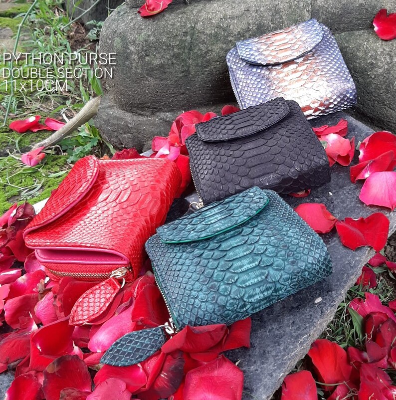 K&ouml;nnte beinhalten: Vier verschiedene farbige Python-Ledergeldb&ouml;rsen mit einem Doppelfach-Design. Die Geldb&ouml;rsen sind 11 x 10 cm gro&szlig; und liegen auf einem Bett aus roten Rosenbl&auml;ttern.