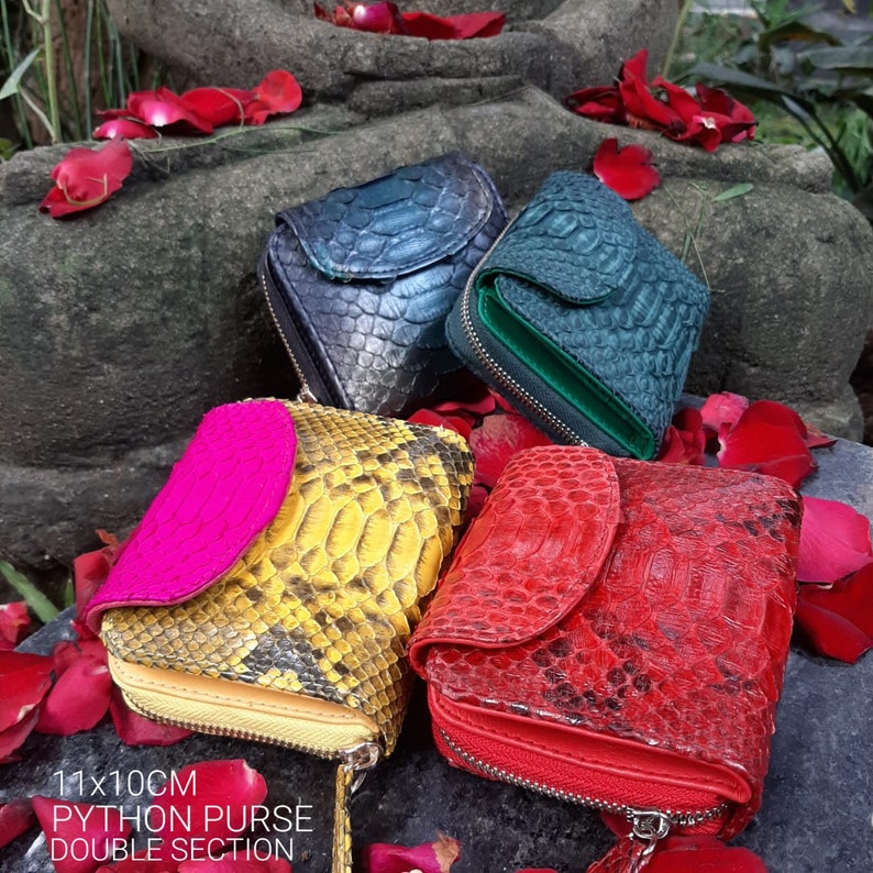 K&ouml;nnte beinhalten: Vier verschiedene Python-Leder-Geldb&ouml;rsen mit Rei&szlig;verschl&uuml;ssen. Die Geldb&ouml;rsen sind in den Farben Gr&uuml;n, Blau, Gelb und Rot gehalten. Die Geldb&ouml;rsen sind auf einer Steinoberfl&auml;che angeordnet, mit roten Bl&uuml;tenbl&auml;ttern, die um sie herum verstreut sind. Der Text "11x10CM PYTHON PURSE DOUBLE SECTION" befindet sich am unteren Rand des Bildes.