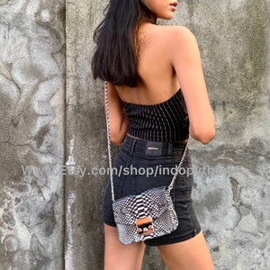 May include: A black and white snakeskin crossbody bag with a silver chain strap and a gold clasp. The bag is worn by a person wearing a black and white striped top and black denim shorts.