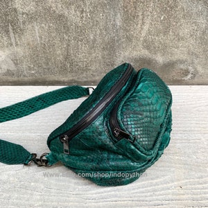 May include: A green snakeskin crossbody bag with a black zipper and a silver chain strap. The bag has a rounded shape and is made of genuine leather.