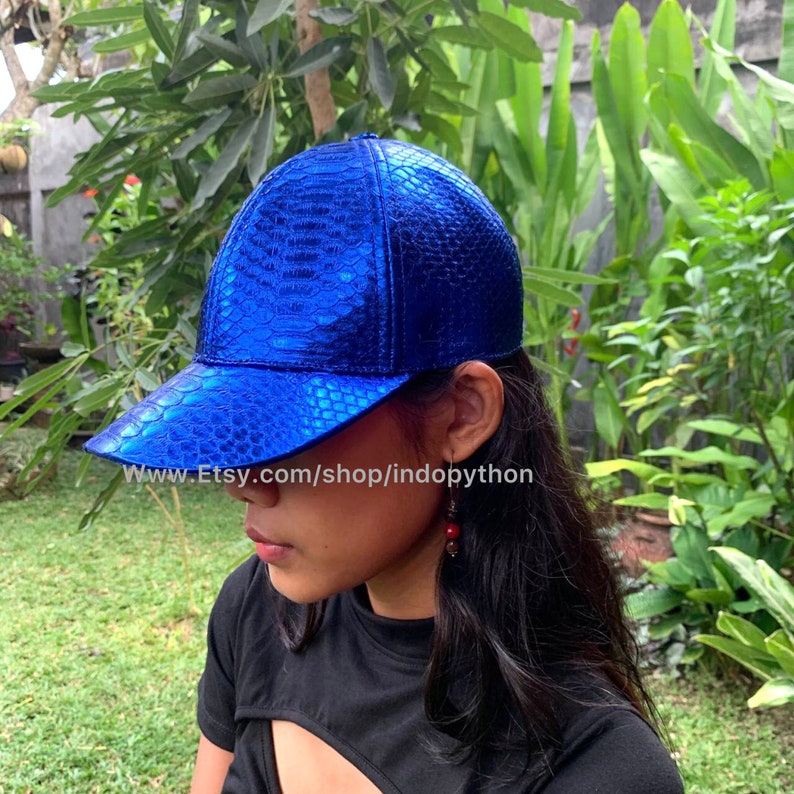 May include: A blue baseball cap made of snakeskin with a shiny, metallic finish. The cap has a curved brim and a structured crown.