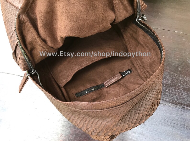 May include: Brown backpack with a textured snakeskin pattern. The bag has a zippered closure and a front pocket. The interior is a lighter brown color. The Etsy shop name is visible in the image.