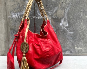 May include: A red python leather handbag with gold braided handles and a gold tassel. The bag has a circular gold emblem with a design on it.