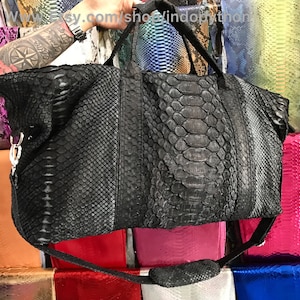 Puede incluir: Bolsa de viaje de cuero negro con estampado de piel de serpiente. La bolsa tiene una correa larga y un asa superior.