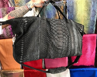 以下が含まれることがあります： ヘビ柄の黒い革製のダッフルバッグ。バッグには長いストラップとトップハンドルが付いています。