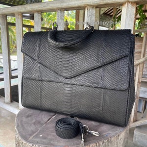 Könnte beinhalten: Schwarze Ledertasche mit Schlangenhautmuster und abnehmbarem Schultergurt. Die Tasche hat zwei obere Griffe und einen silbernen Verschluss.