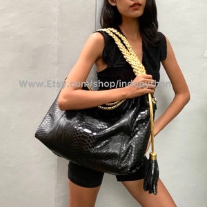 May include: A black python leather tote bag with a gold chain strap and tassel. The bag has a textured snakeskin pattern and a spacious interior.