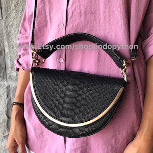 Può includere: Una borsa a mano in pelle nera con motivo a pelle di serpente e dettagli dorati. La borsa ha un manico superiore e una tracolla.