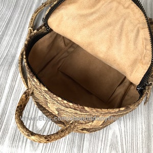 May include: Open view of a brown and tan snakeskin backpack with a black zipper. The interior is lined with tan fabric and includes a small pocket. The bag has a top handle and adjustable straps.