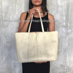 May include: A large, off-white tote bag made of snakeskin. The bag has a structured shape and two top handles.