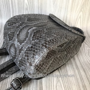 K&ouml;nnte beinhalten: Ein grauer Schlangenleder-Rucksack mit Rei&szlig;verschluss und verstellbaren Tr&auml;gern. Der Rucksack ist aus echtem Leder gefertigt und hat ein einzigartiges, strukturiertes Design.