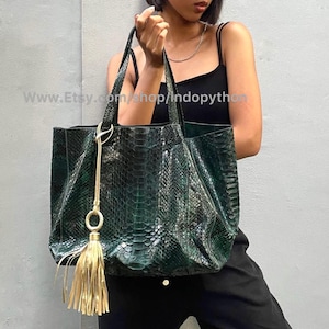May include: A green snakeskin tote bag with a gold tassel. The bag has a top zipper closure and two top handles.
