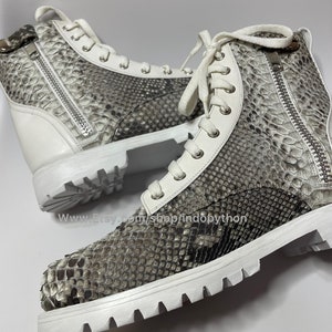 May include: White leather high-top sneakers with a snakeskin pattern and white laces. The sneakers have a zipper on the side and a white rubber sole.