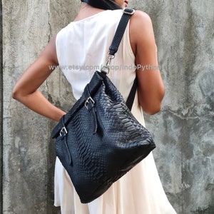 Peut inclure: Un sac &agrave; main en cuir noir avec un motif en peau de serpent et des boucles argent&eacute;es. Le sac a une longue bandouli&egrave;re et est port&eacute; &agrave; l'&eacute;paule.