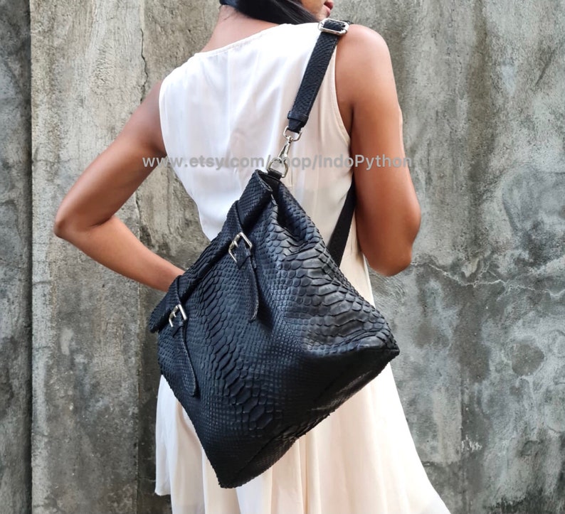 Peut inclure: Un sac &agrave; main en cuir noir avec un motif en peau de serpent et des boucles argent&eacute;es. Le sac a une longue bandouli&egrave;re et est port&eacute; &agrave; l'&eacute;paule.