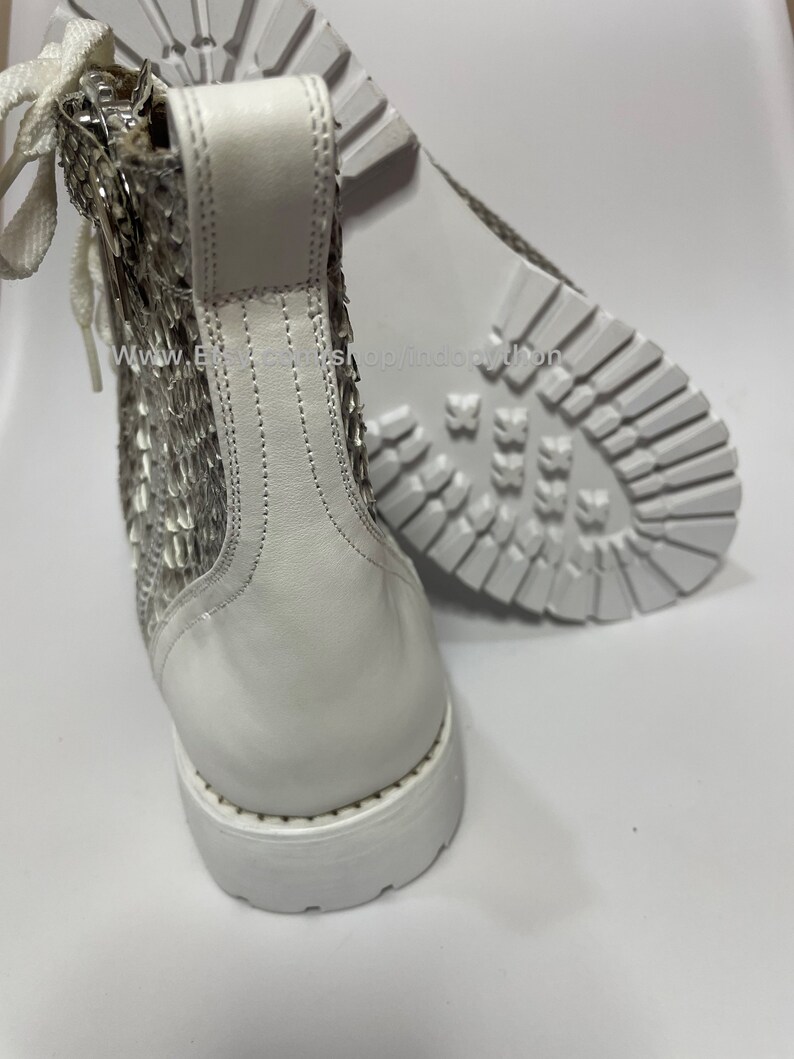 May include: White leather ankle boots with a snakeskin pattern on the back of the boot. The boots have a white rubber sole.