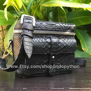 Może przedstawiać: Czarna skórzana torebka na ramię z pytona z srebrnym zamkiem błyskawicznym i klamrą. Torebka ma małą kieszeń z przodu i pasek ze srebrną klamrą. Torebka leży na drewnianej powierzchni. www.Etsy.com/shop/indopython