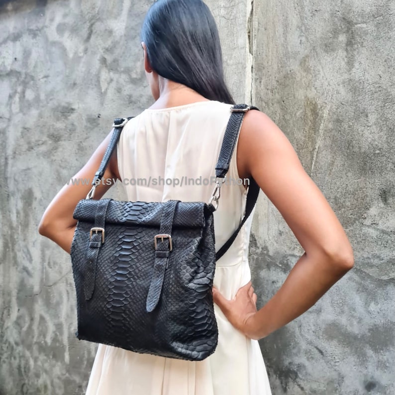 Peut inclure: Un sac &agrave; dos en cuir noir avec une fermeture &agrave; rabat et des accents de boucle. Le sac est en peau de serpent et poss&egrave;de une longue sangle r&eacute;glable.