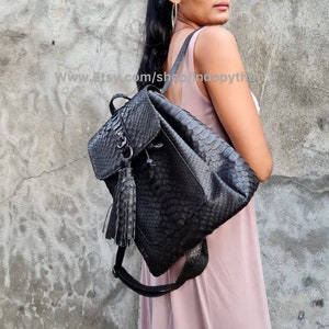 May include: Black leather backpack with a snakeskin pattern and a tassel. The backpack has a drawstring closure and a flap with a buckle.