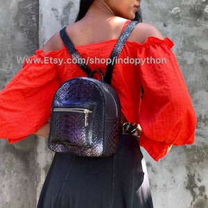 May include: A black, textured backpack with a rounded shape and a front zippered pocket. The backpack has adjustable straps and a small top handle. The text "www.Etsy.com/shop/indopython" is visible on the image.