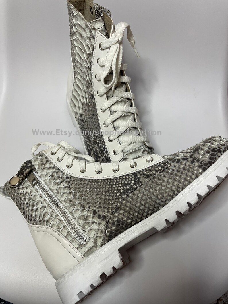 May include: White leather boots with a snakeskin pattern and white laces. The boots have a zipper on the side and a thick white sole.