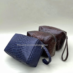 Peut inclure: Trois sacs en cuir de différentes tailles avec un motif en peau de serpent. Les sacs sont dans des tons de bleu, marron et marron foncé. Les sacs ont des fermetures à glissière et une poignée.