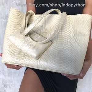 May include: A large, off-white, snakeskin tote bag with a smaller matching snakeskin clutch. The tote bag has two top handles and a zipper closure.