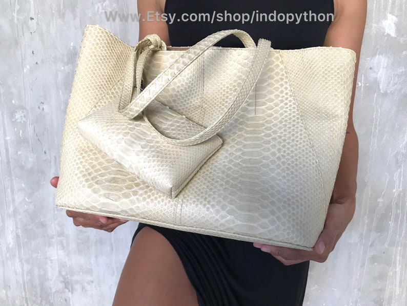 May include: A large, off-white, snakeskin tote bag with a smaller matching snakeskin clutch. The tote bag has two top handles and a zipper closure.