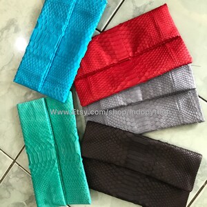 Peut inclure: Plusieurs pochettes de soir&eacute;e rectangulaires, de couleurs turquoise, rouge, grise, marron et vert d'eau. Chaque pochette pr&eacute;sente un rabat et une texture &agrave; motifs d'&eacute;cailles. Le texte sur l'image indique : www.etsy.com/shop/indopython. Elles sont faites d'un mat&eacute;riau semblable &agrave; de la peau de serpent.