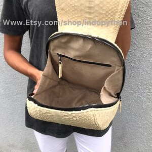 May include: A beige python leather backpack with a zipper closure and a small pocket inside. The backpack is open and the interior is visible. The website www.Etsy.com/shop/indopython is printed on the leather.