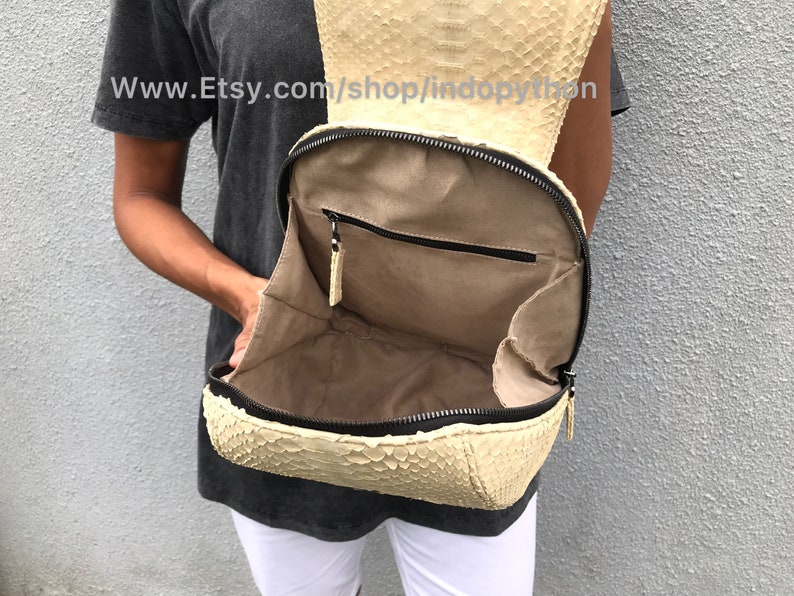 May include: A beige python leather backpack with a zipper closure and a small pocket inside. The backpack is open and the interior is visible. The website www.Etsy.com/shop/indopython is printed on the leather.