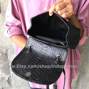 May include: Black leather handbag with a snakeskin pattern. The bag is open and the inside is lined with black fabric. The bag has a zipper closure and a drawstring closure.