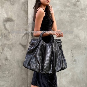 May include: A large black snakeskin tote bag with a structured shape and a top handle. The bag is made of genuine python skin and has a sleek, modern design.