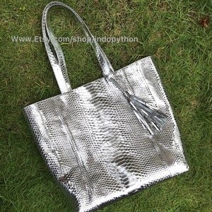 May include: A silver snakeskin tote bag with a tassel. The bag has a top zipper closure and two top handles.