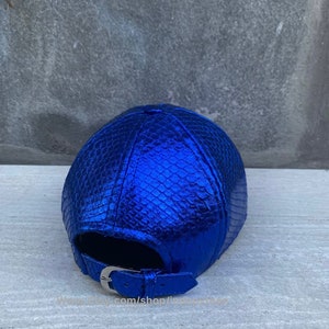 May include: A blue metallic baseball cap with a snakeskin pattern. The cap has a silver buckle closure.