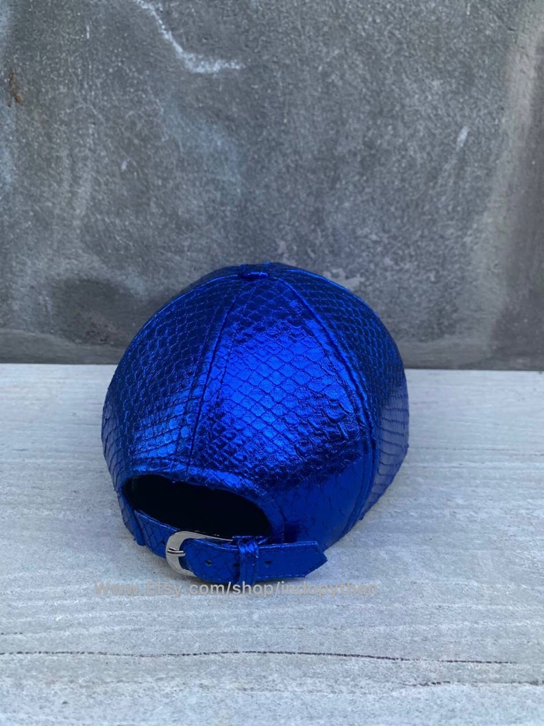 May include: A blue metallic baseball cap with a snakeskin pattern. The cap has a silver buckle closure.