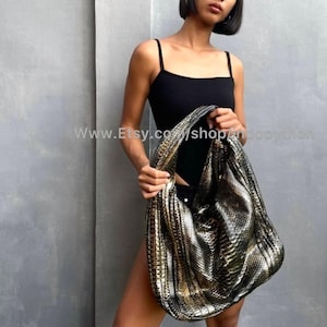 Peut inclure: Un grand sac à bandoulière métallique or et argent avec un motif peau de serpent. Le sac est tenu par une personne portant un haut noir. L'adresse du site Web www.Etsy.com/shop/andpython est visible sur l'image.